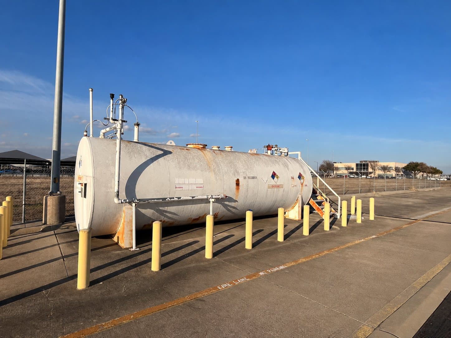 Older aboveground fuel tank with protective bollards at a fueling facility.